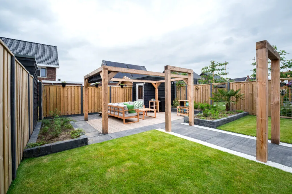 Achtertuin met houten pergola, loungeset, gazon, donkere berging en losstaand houten poortframe