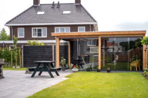 Achtertuin met glazen buitenverblijf tegen de gevel, picknickbank op het terras en gazon