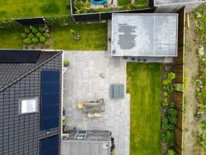 Drone-opname van een achtertuin met grijs terras, gazonvlakken, plantvakken en zonnepanelen op het dak