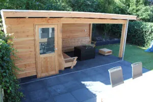 Houten overkapping aan een woning met loungehoek, donkere terrastegels en ligstoelen op het terras